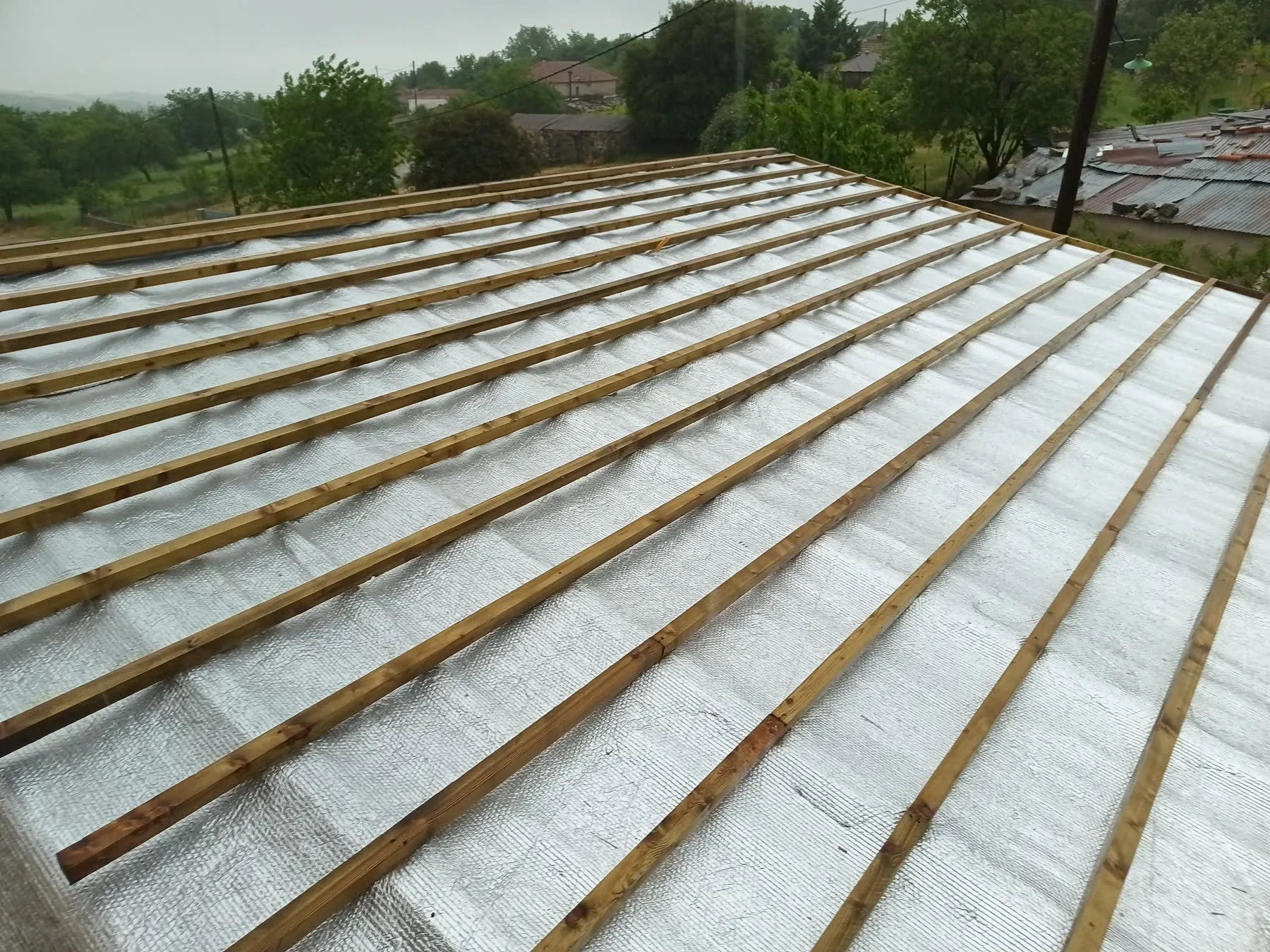 A reflective waterproof membrane over roof insulation with tile battens fixed above it, in rain