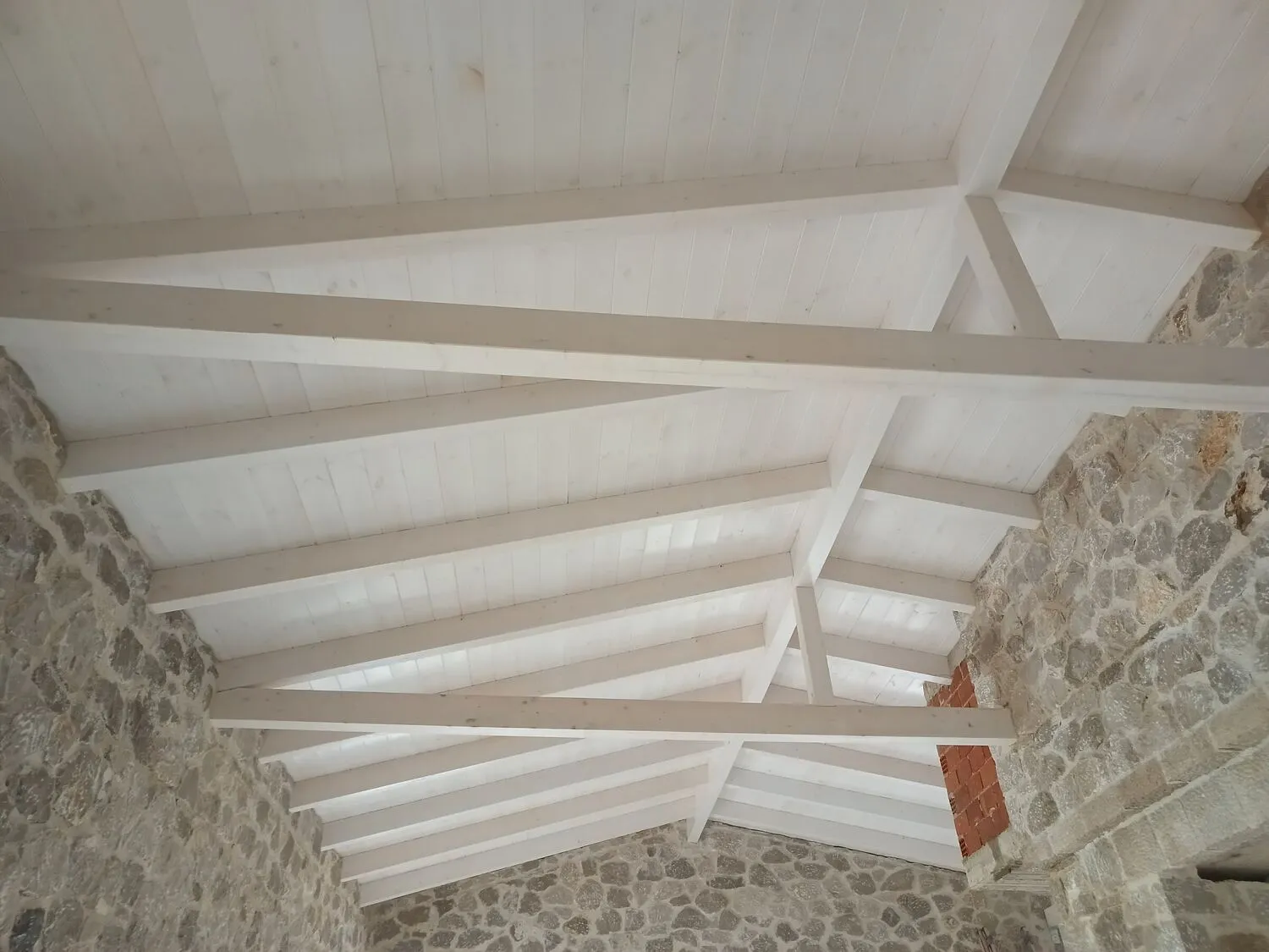 Interior view of the finished timber ceiling with exposed beams against stone walls