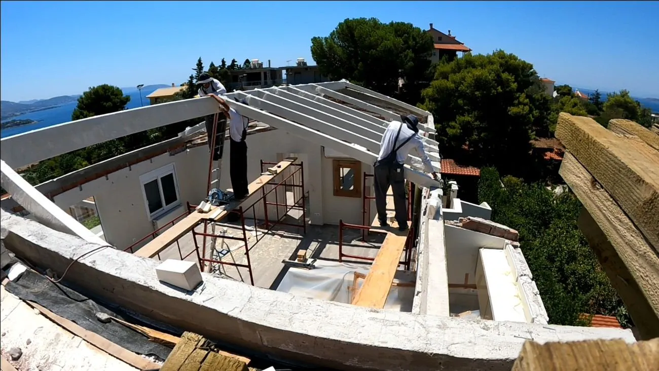 The new GL24 glulam skeleton, workers at height, the Athenian Riviera and Saronic Gulf behind.