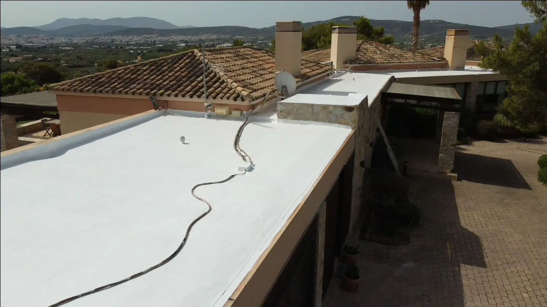A completed terrace finished in white liquid-applied waterproofing on a premium residence, tiled roofs and hills behind